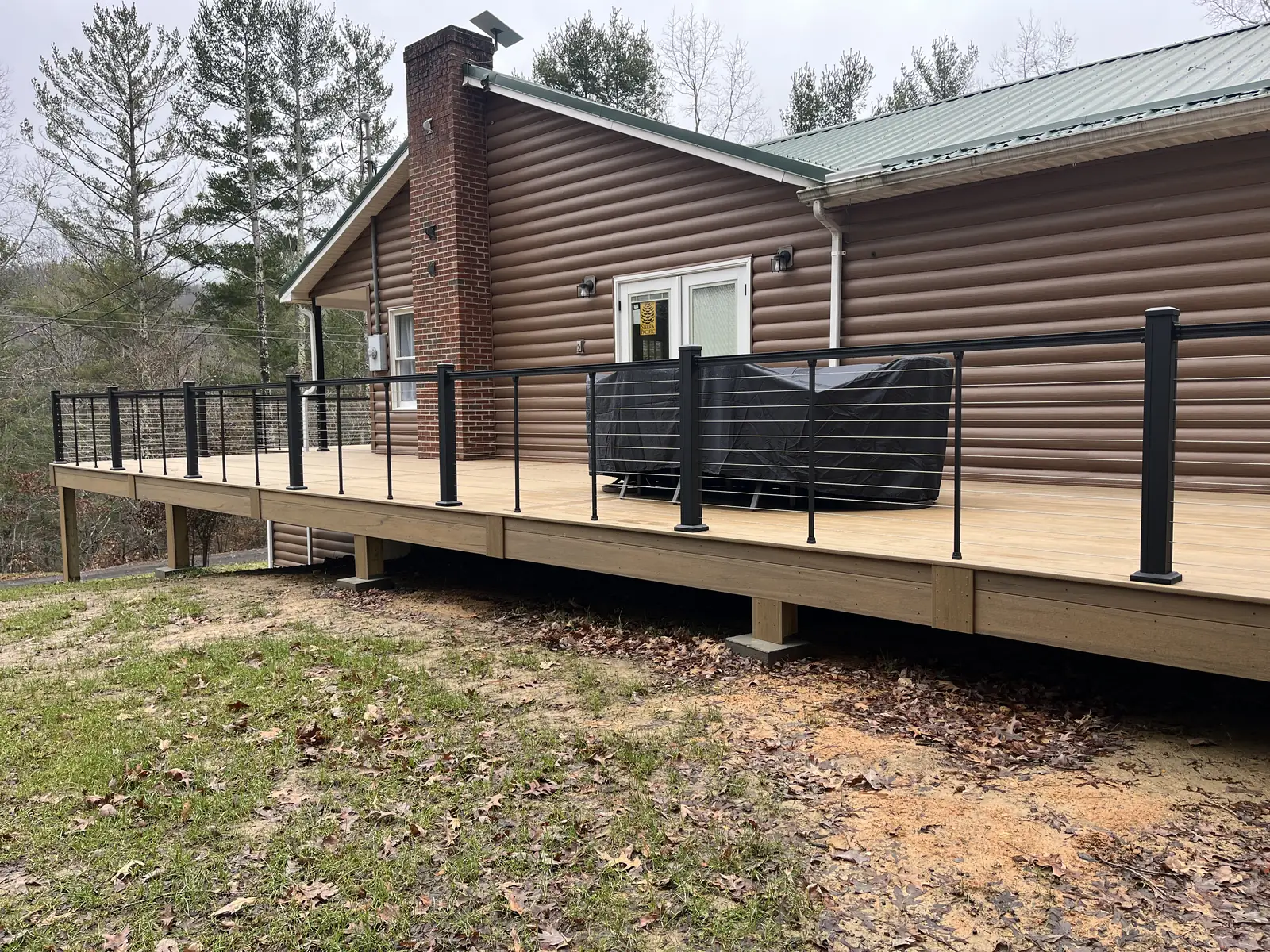 Tan composite deck with black cable railing at a log cabin