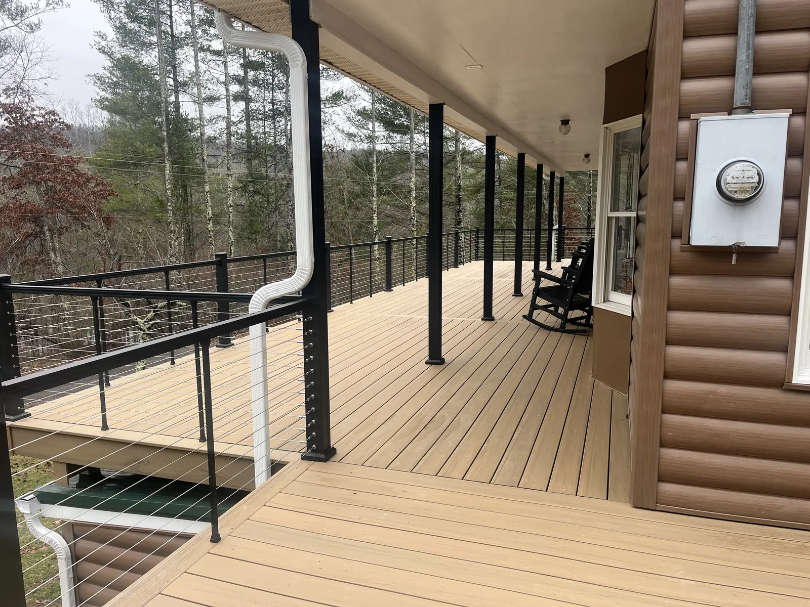 Homeowner relaxing on a tan composite deck with cable railing at the forest edge