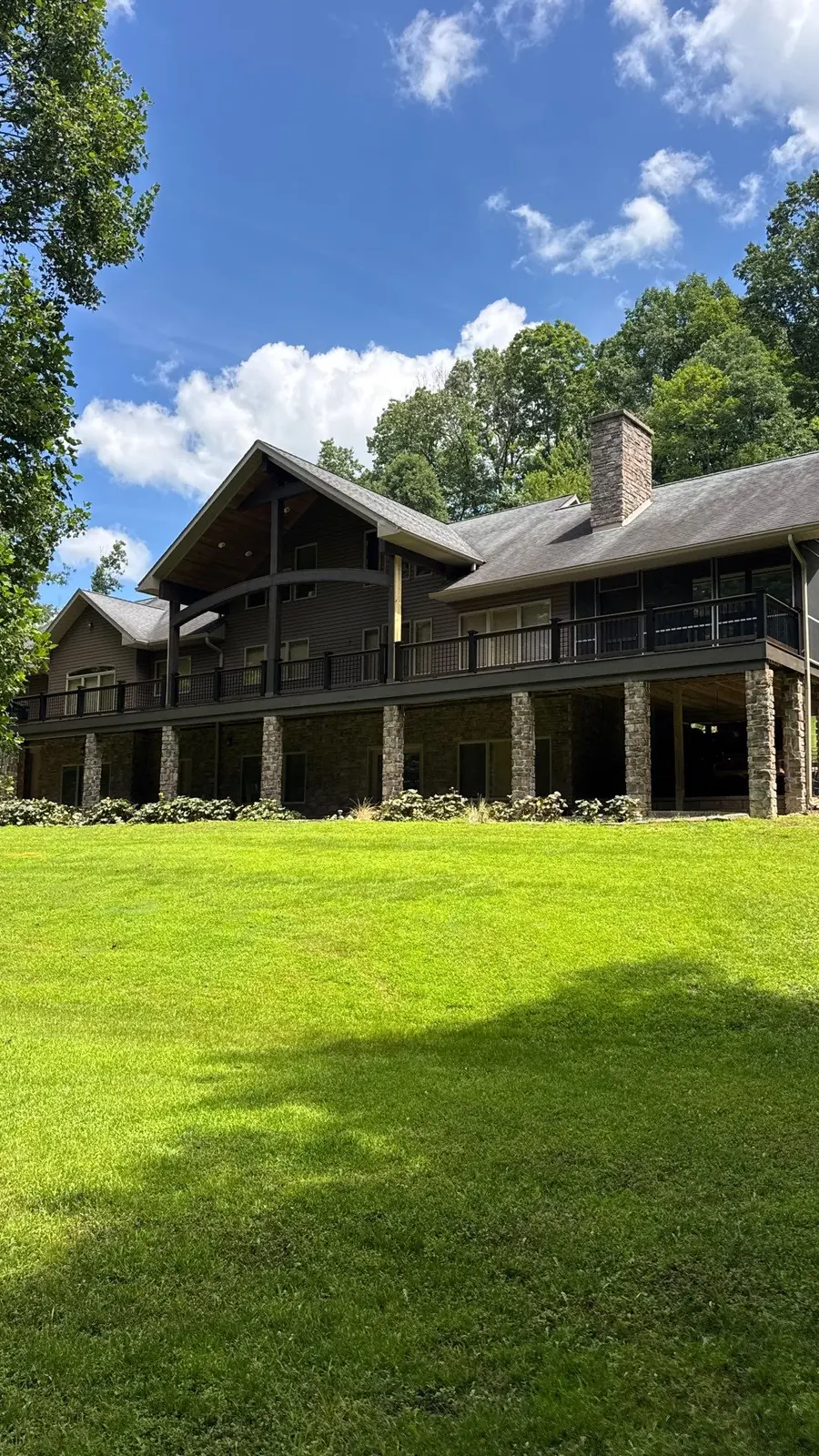Wraparound composite deck with black railing on stone pillars behind a mountain home
