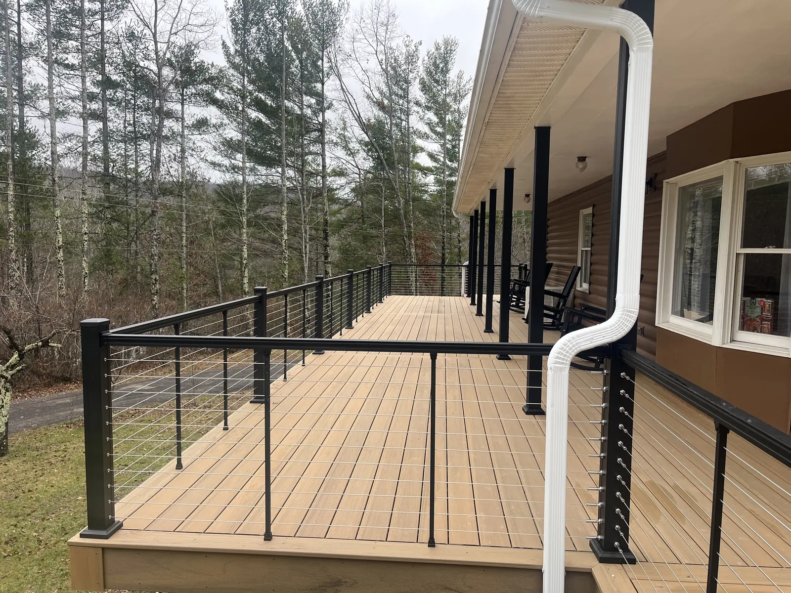 Multi-level tan composite deck with black cable railing overlooking the woods