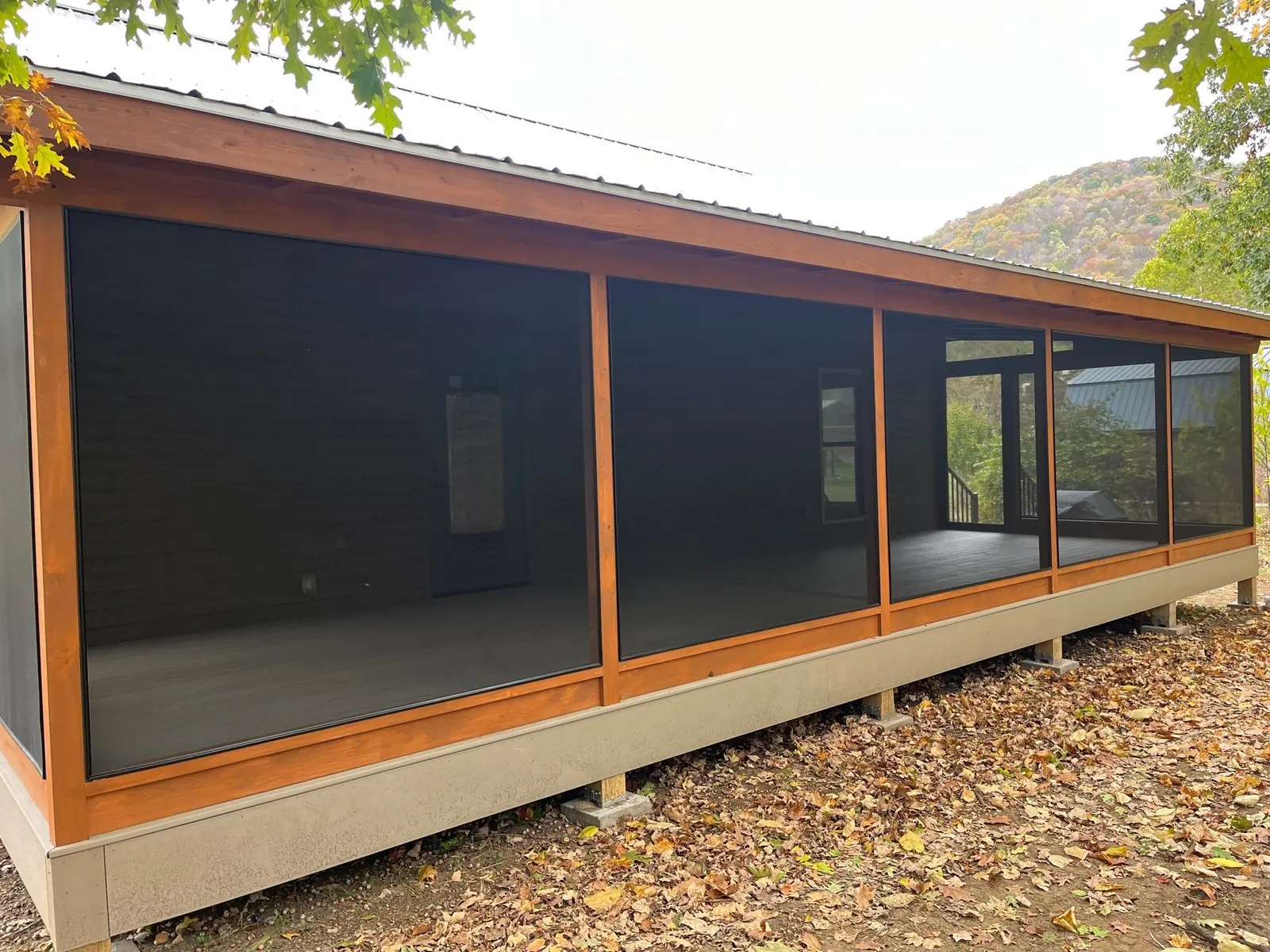Screened porch exterior with black mesh panels on a wooded hillside