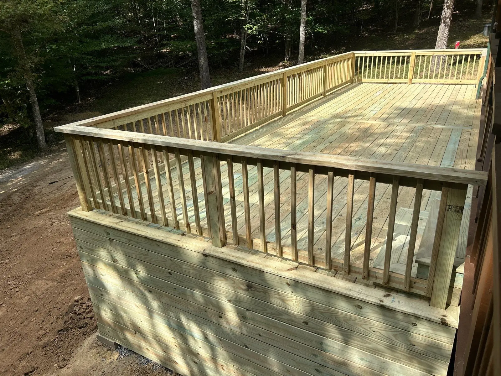 Raised wood deck with spindle railing and skirting on a wooded hillside